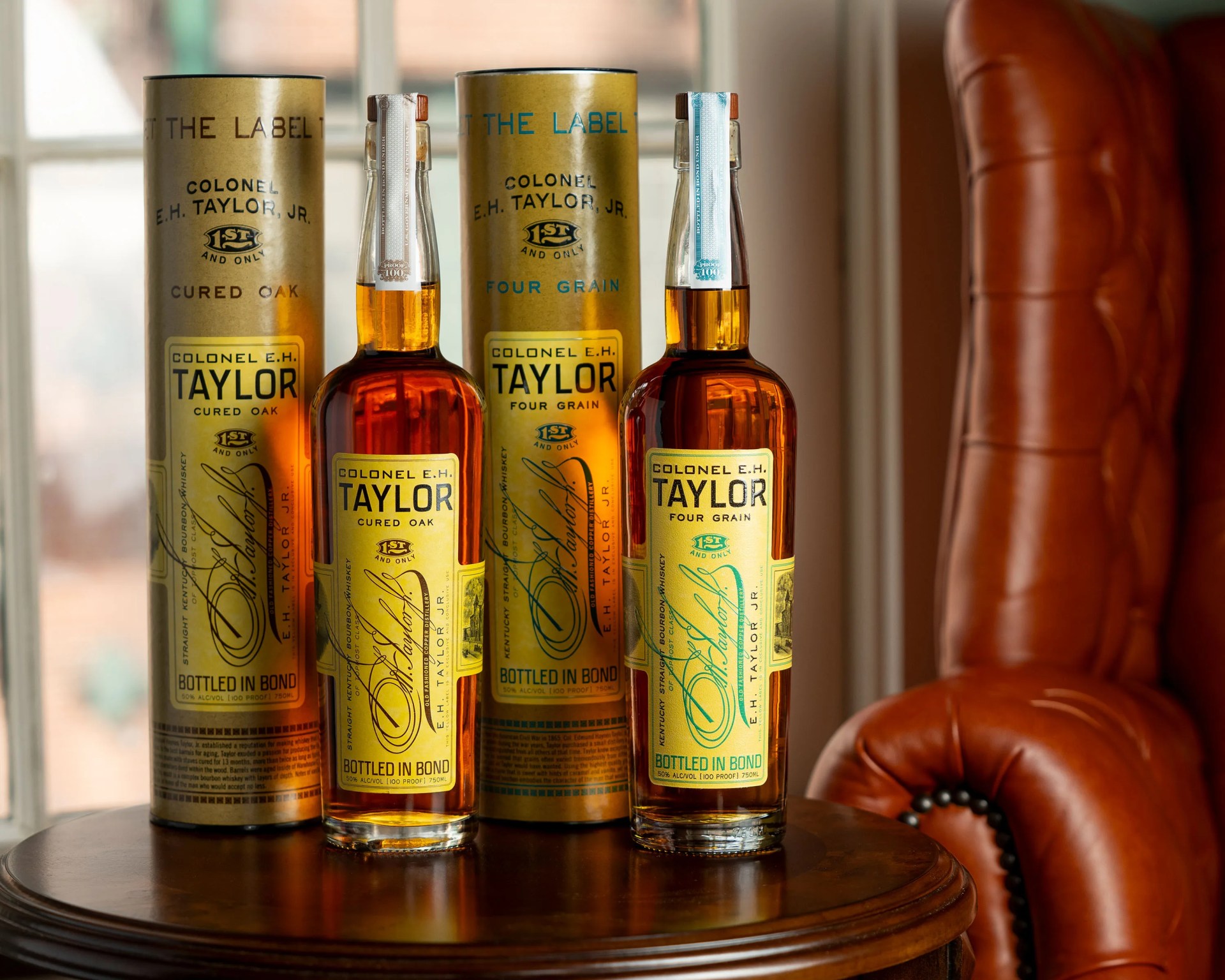 Two bottles of Colonel E.H. Taylor bourbon whiskey with matching cylindrical boxes on a wooden table.