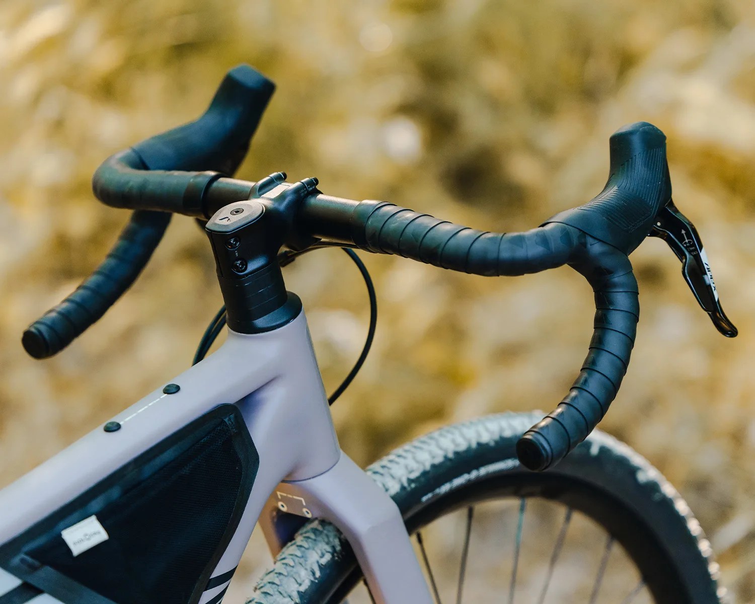 Close-up of a gray bicycle frame with black drop handlebars wrapped in black tape and a knobby tire.