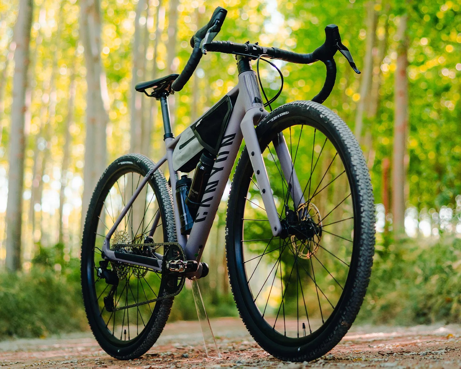 Matte gray Canyon gravel bike with drop handlebars and two water bottles on a forest trail.