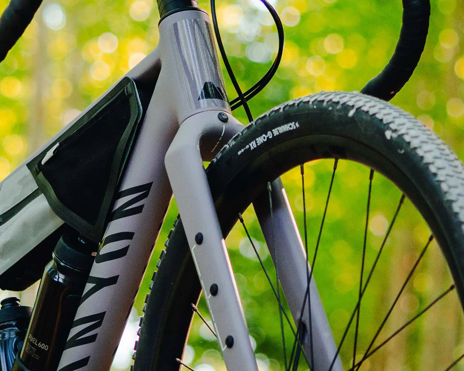 Close-up of a gray Canyon bike frame with a black water bottle, black frame bag, and knobby Schwalbe G-One tire.