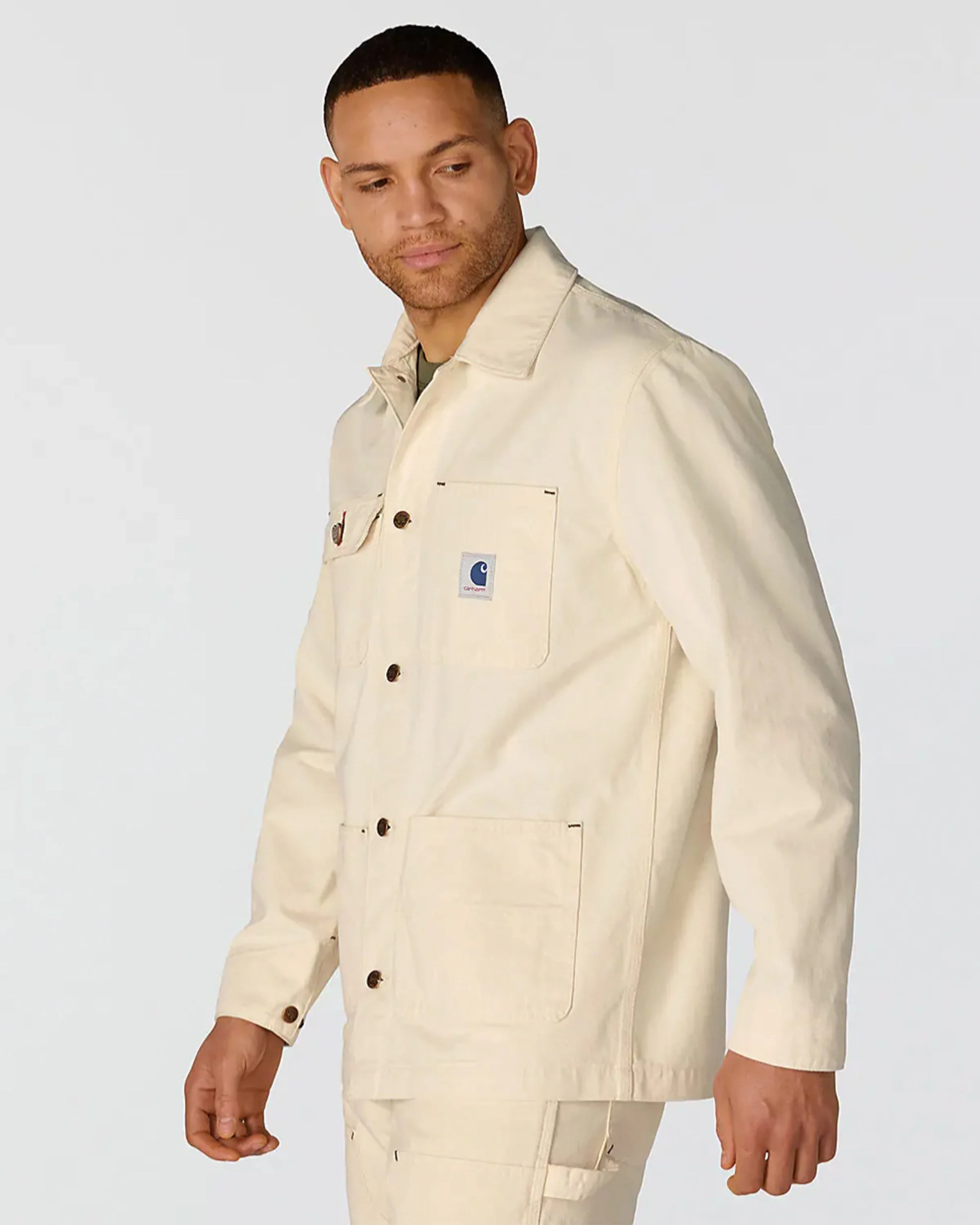 Beige Carhartt jacket with buttoned front and chest pocket worn by a person.