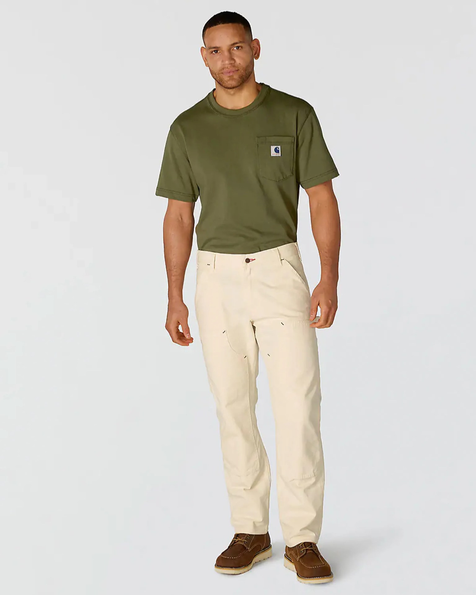 Man wearing an olive green short-sleeve pocket t-shirt, cream pants, and brown leather shoes.