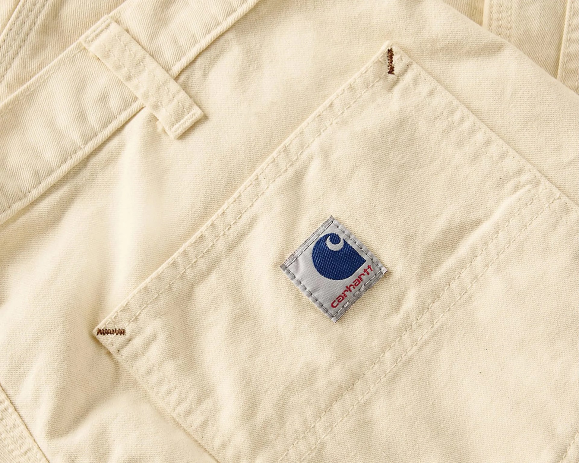 Close-up of beige Carhartt fabric with a stitched pocket and logo patch.