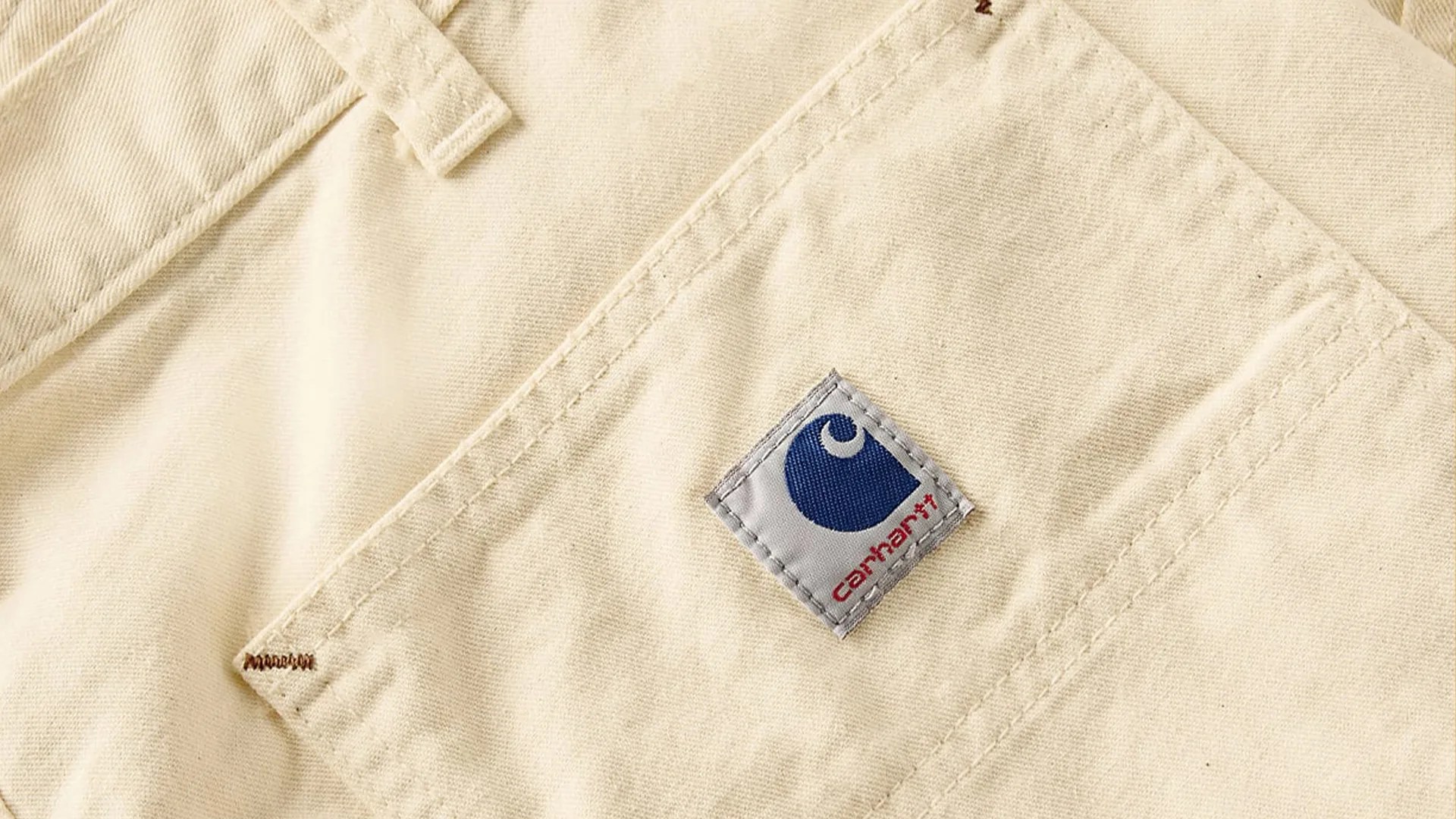 Close-up of beige fabric with a stitched Carhartt logo patch in blue and red.