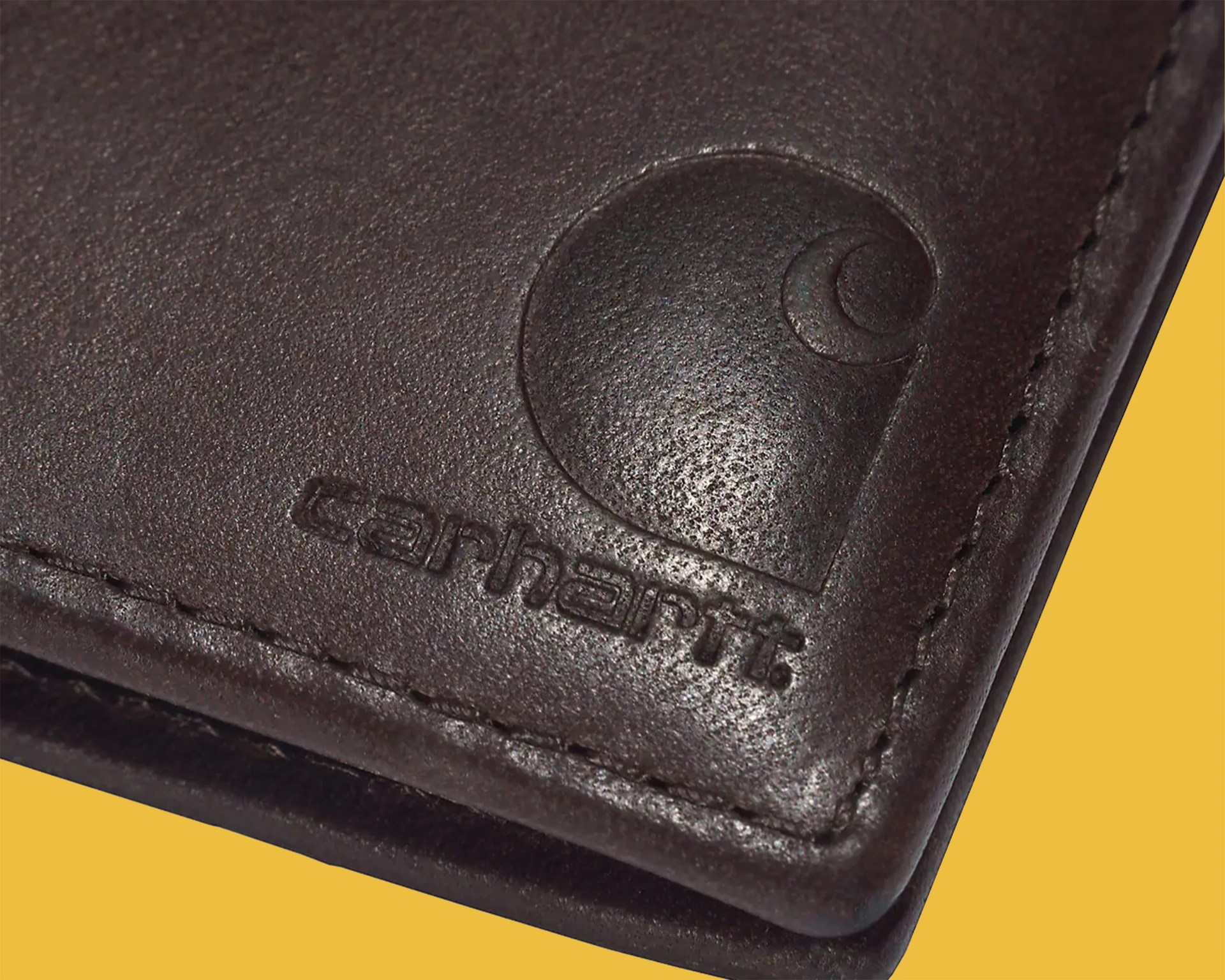 Close-up of dark brown leather with embossed Carhartt logo and stitching on a yellow background.