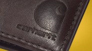 Close-up of dark brown leather with embossed Carhartt logo and stitching on a yellow background.