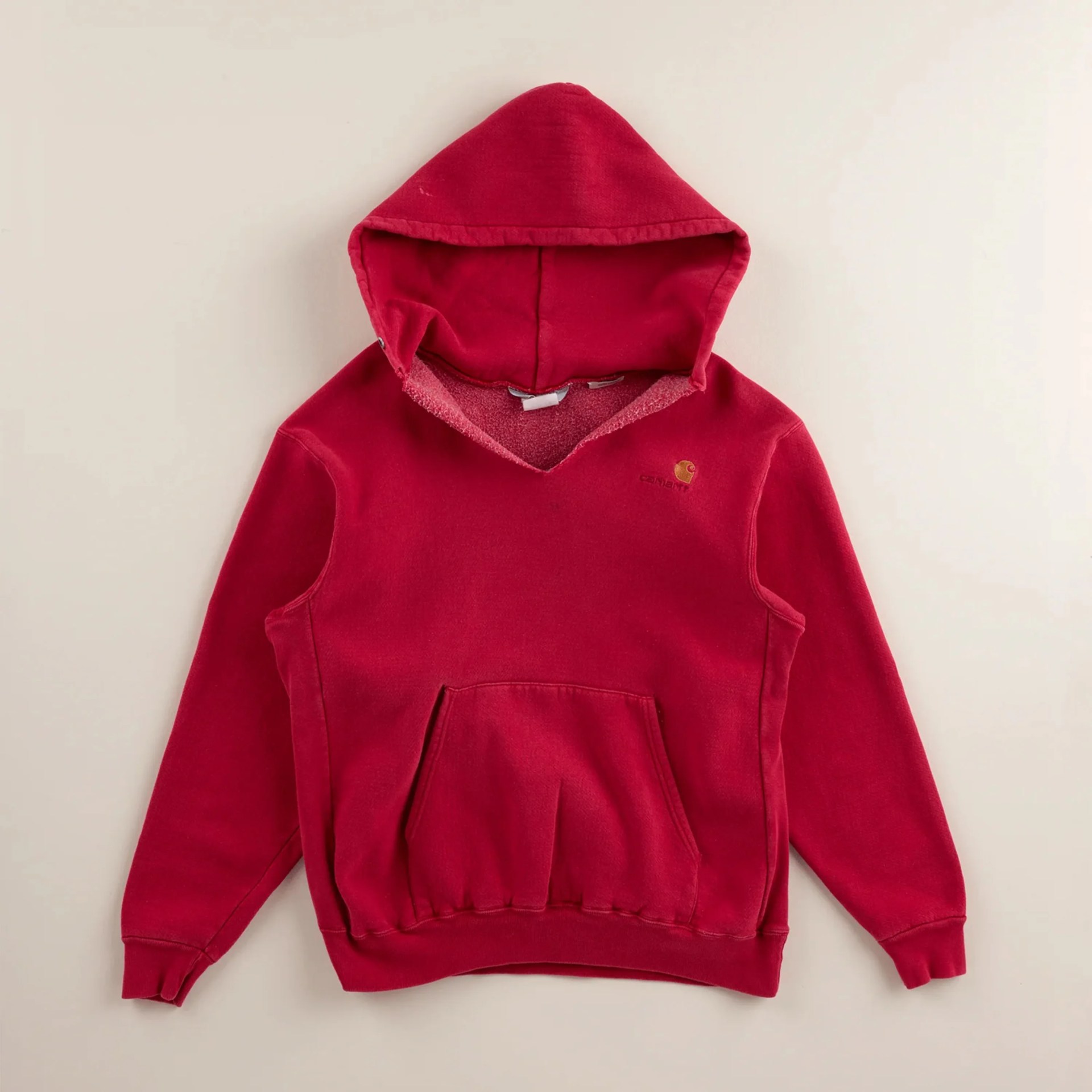 Red Carhartt hooded sweatshirt with front pocket and ribbed cuffs and hem laid flat on a light surface.