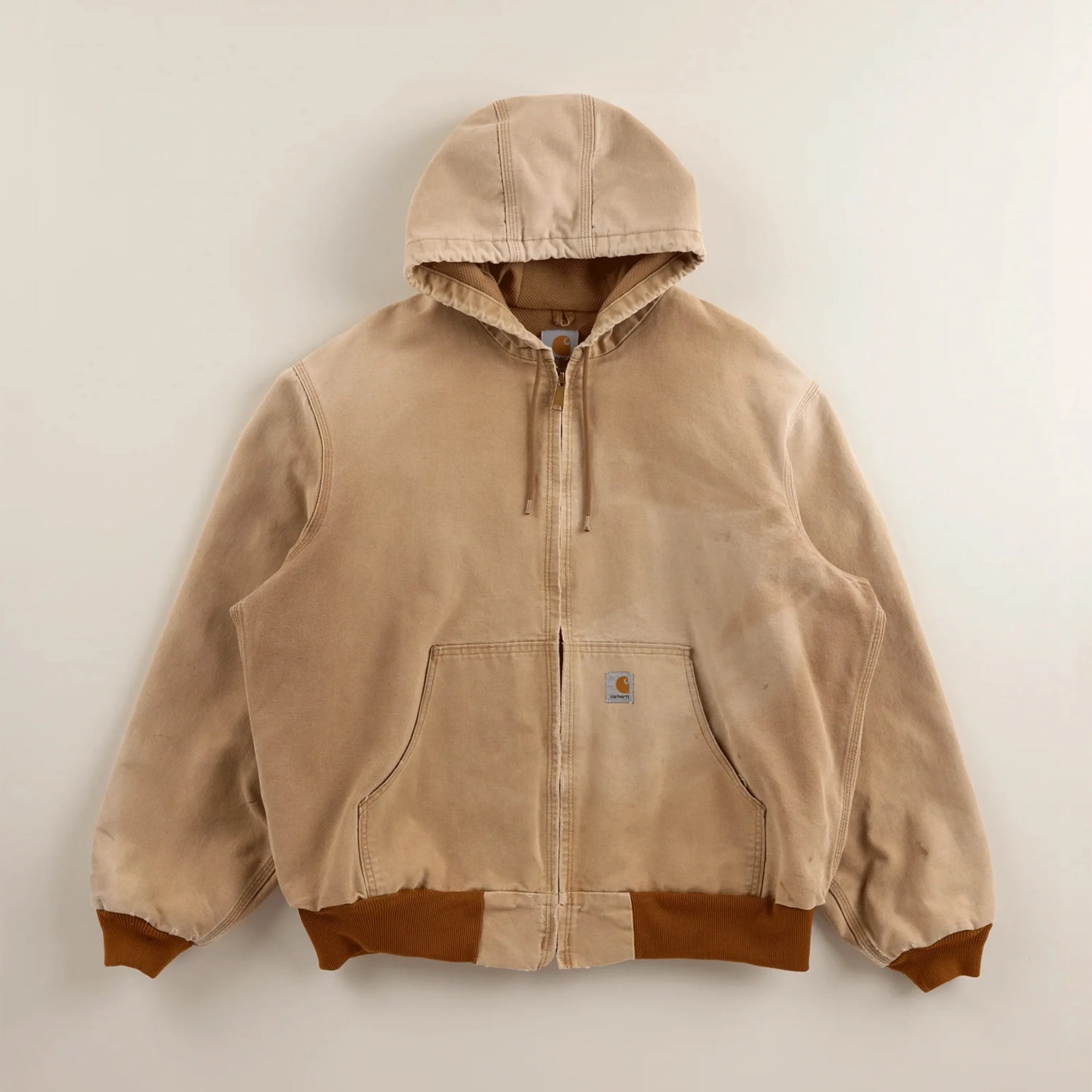 Beige Carhartt hooded jacket with front zipper, kangaroo pocket, and brown ribbed cuffs and hem.