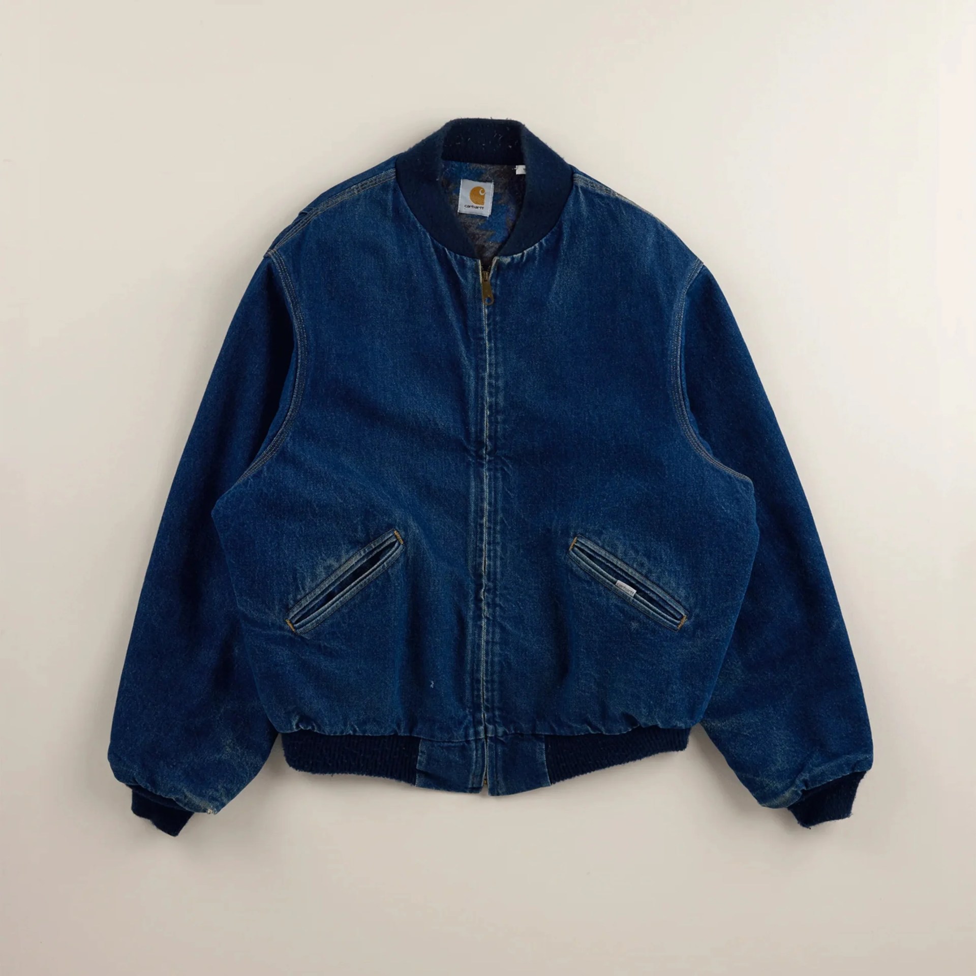 Dark blue denim bomber jacket with ribbed collar, cuffs, and waistband, featuring zippered front pockets.