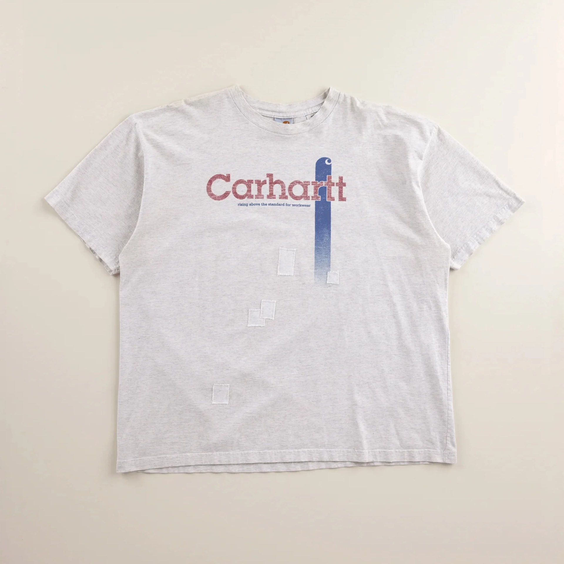 Light gray Carhartt T-shirt with red and blue logo and small white stitched patches on front.