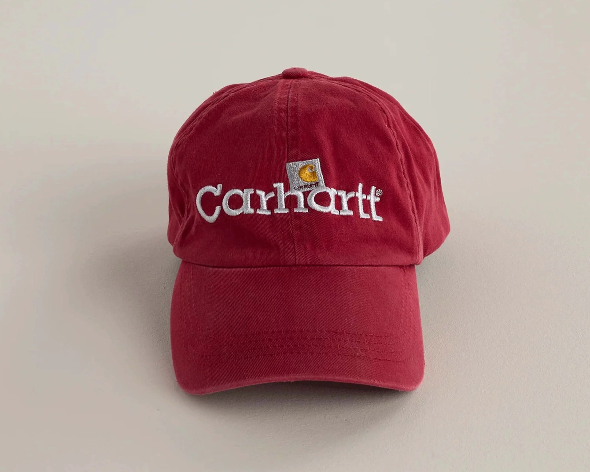 Red Carhartt baseball cap with white embroidered logo on front against a plain light background.