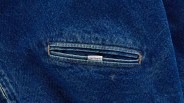 Close-up of a blue denim fabric with a small horizontal slit pocket featuring a white Carhartt label.