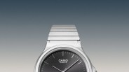 Silver Casio quartz watch with black dial and metal link band against gradient background.