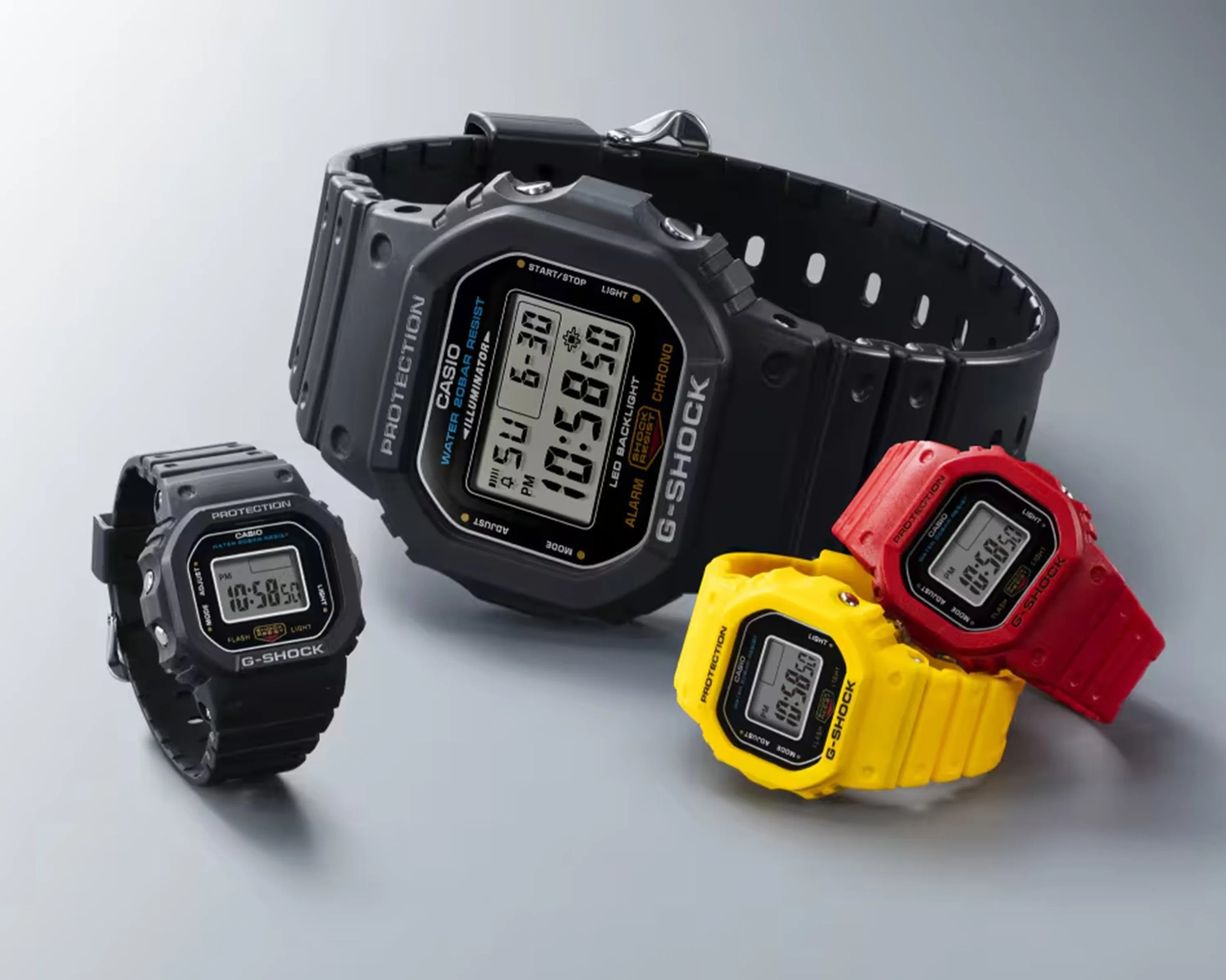 Four Casio G-Shock digital watches in black, red, and yellow with rectangular faces on a gray surface.