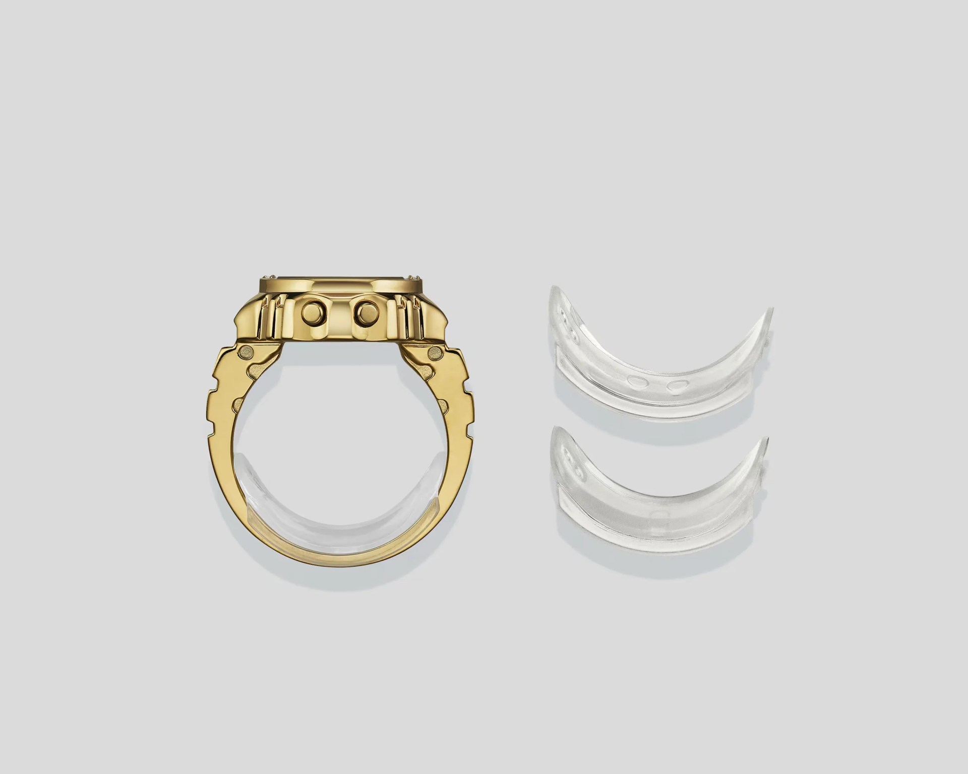 Gold watch case with two buttons on the side and three clear plastic curved inserts on a gray background.