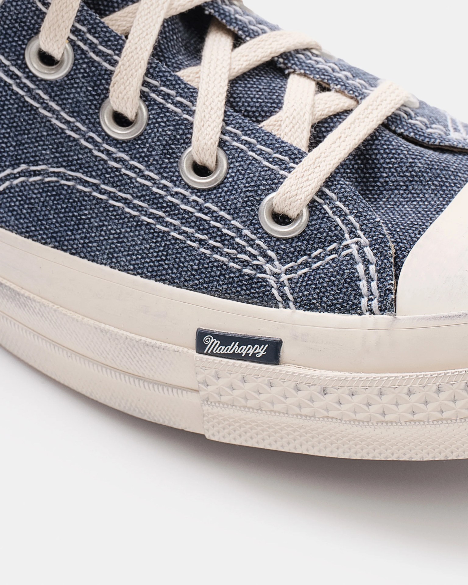 Close-up of navy blue canvas sneaker with white laces and white rubber sole labeled "Madhappy.