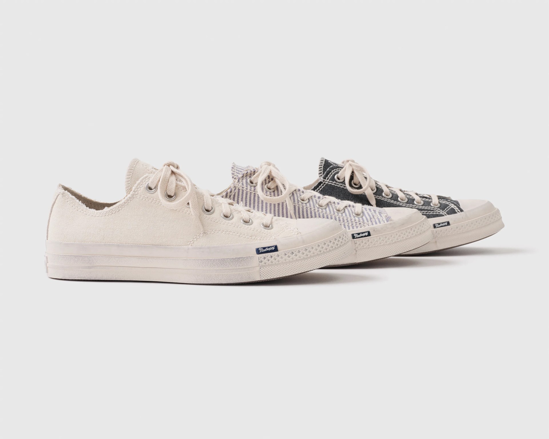Three pairs of low-top canvas sneakers in cream, striped blue and white, and black colors, arranged in a row.