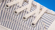 Close-up of beige and blue striped fabric sneaker with beige laces threaded through silver eyelets.