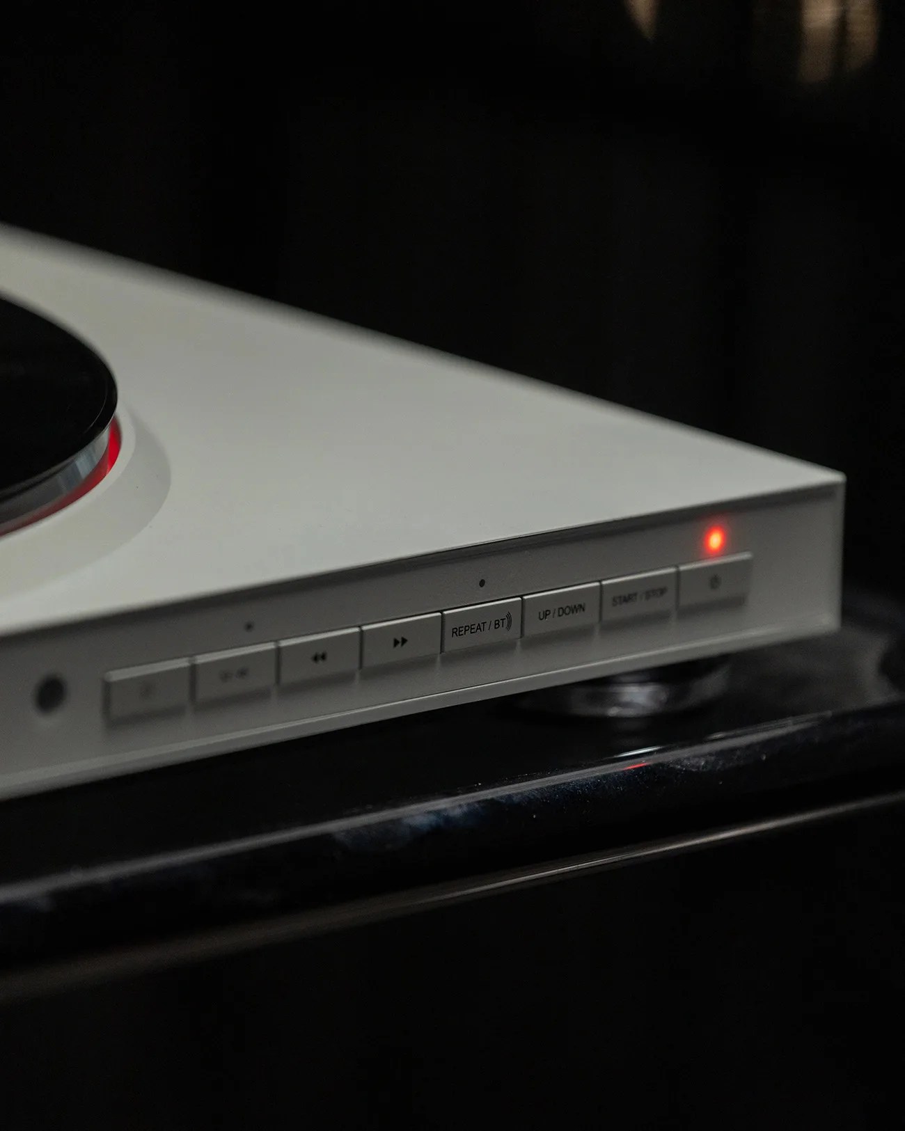 Close-up of a white electronic device with buttons labeled "REPEAT/BT," "UP/DOWN," and "START/STOP," with a red indicator light on.