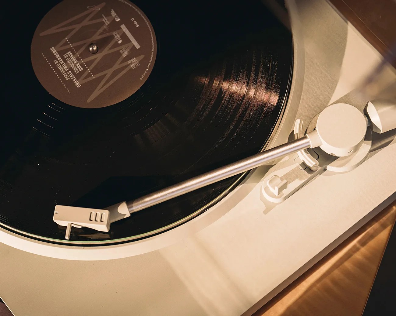 Close-up of a black vinyl record on a beige turntable with a silver tonearm and white cartridge.