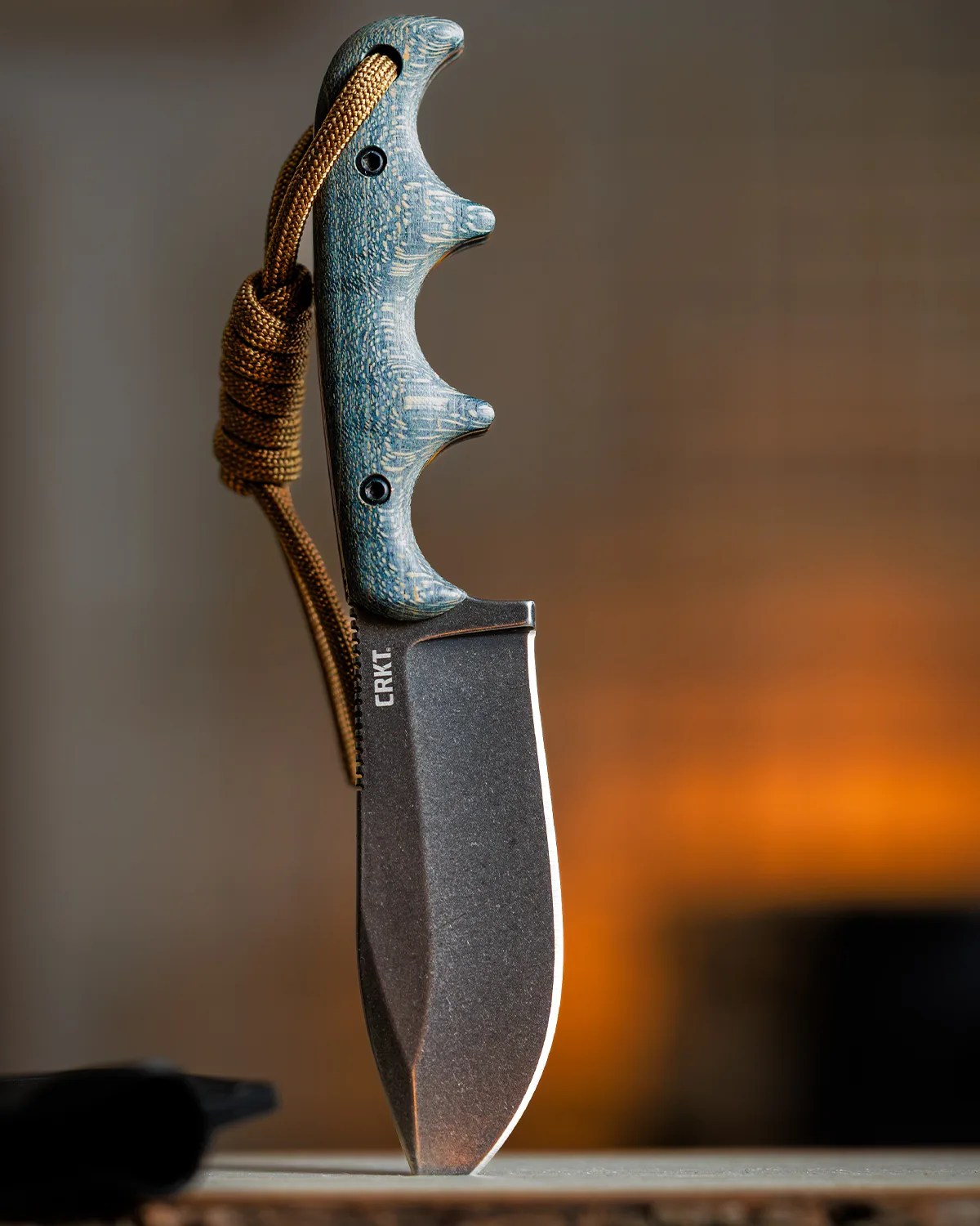 Fixed-blade CRKT knife with textured blue handle and brown lanyard looped through it.