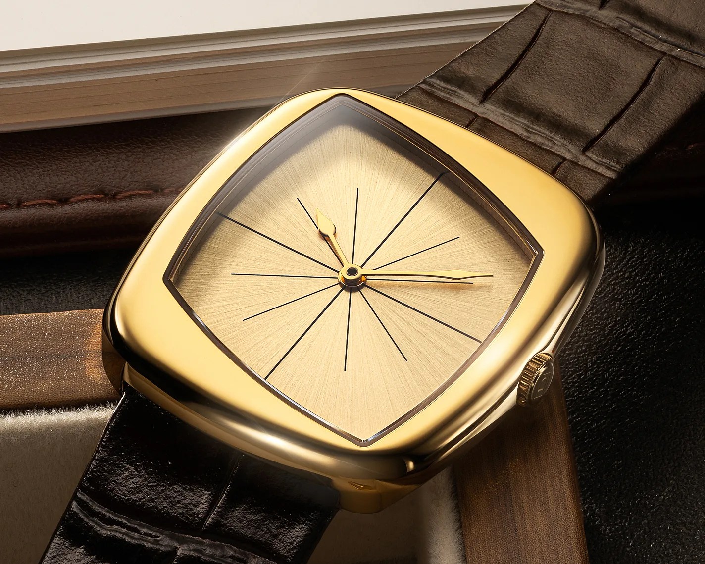 Gold square wristwatch with sunburst dial and black leather strap on a textured surface.