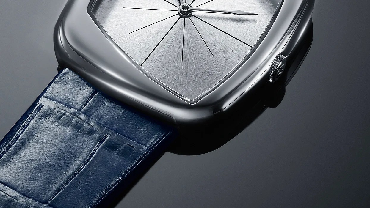 Close-up of a silver watch with a triangular brushed metal dial and a blue leather strap.