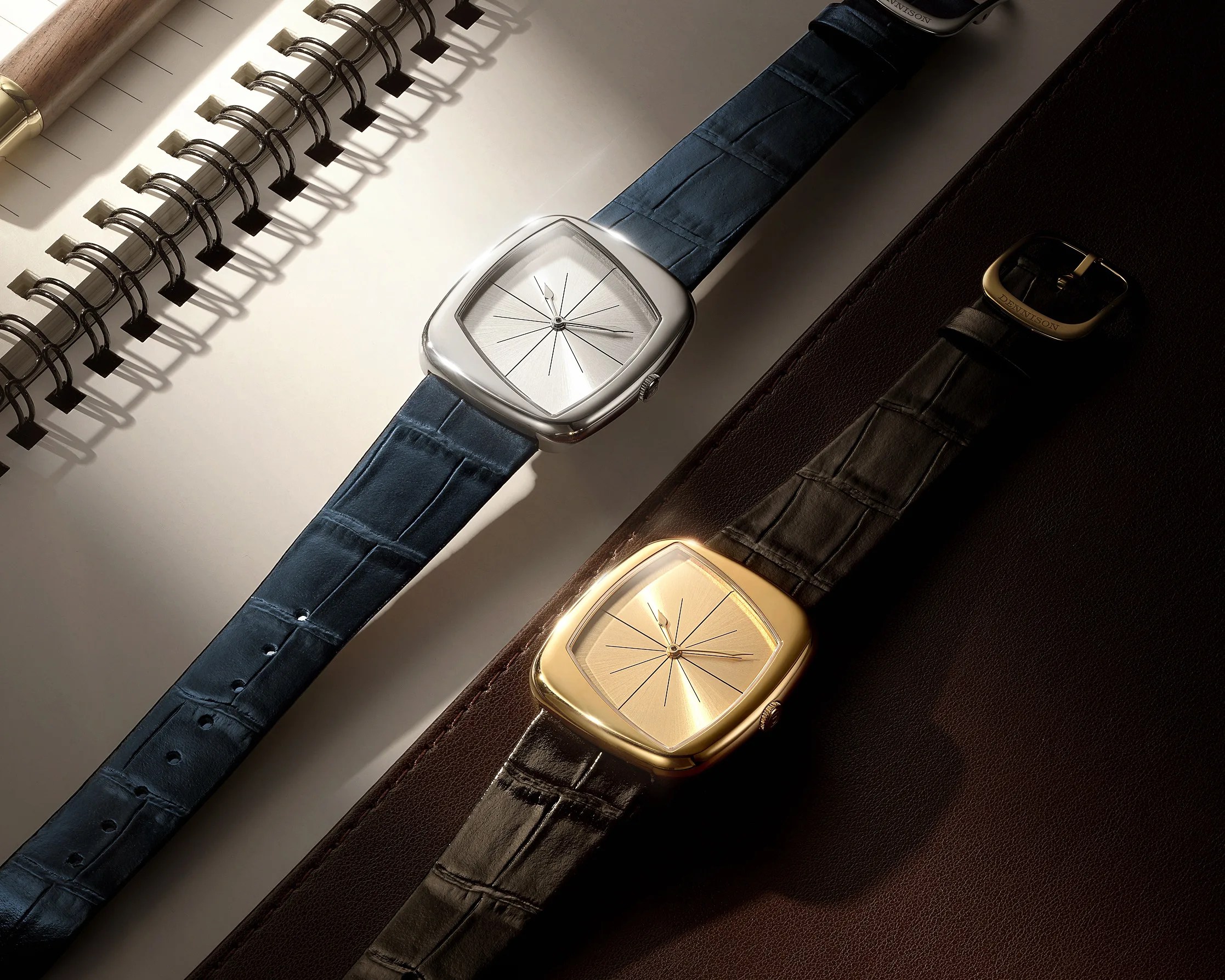 Two square-faced wristwatches with sunburst dials, one silver with a blue leather strap and one gold with a black leather strap.