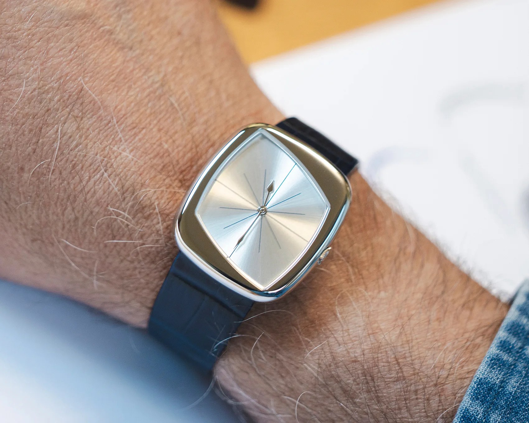 Silver square-faced wristwatch with black strap worn on a wrist.