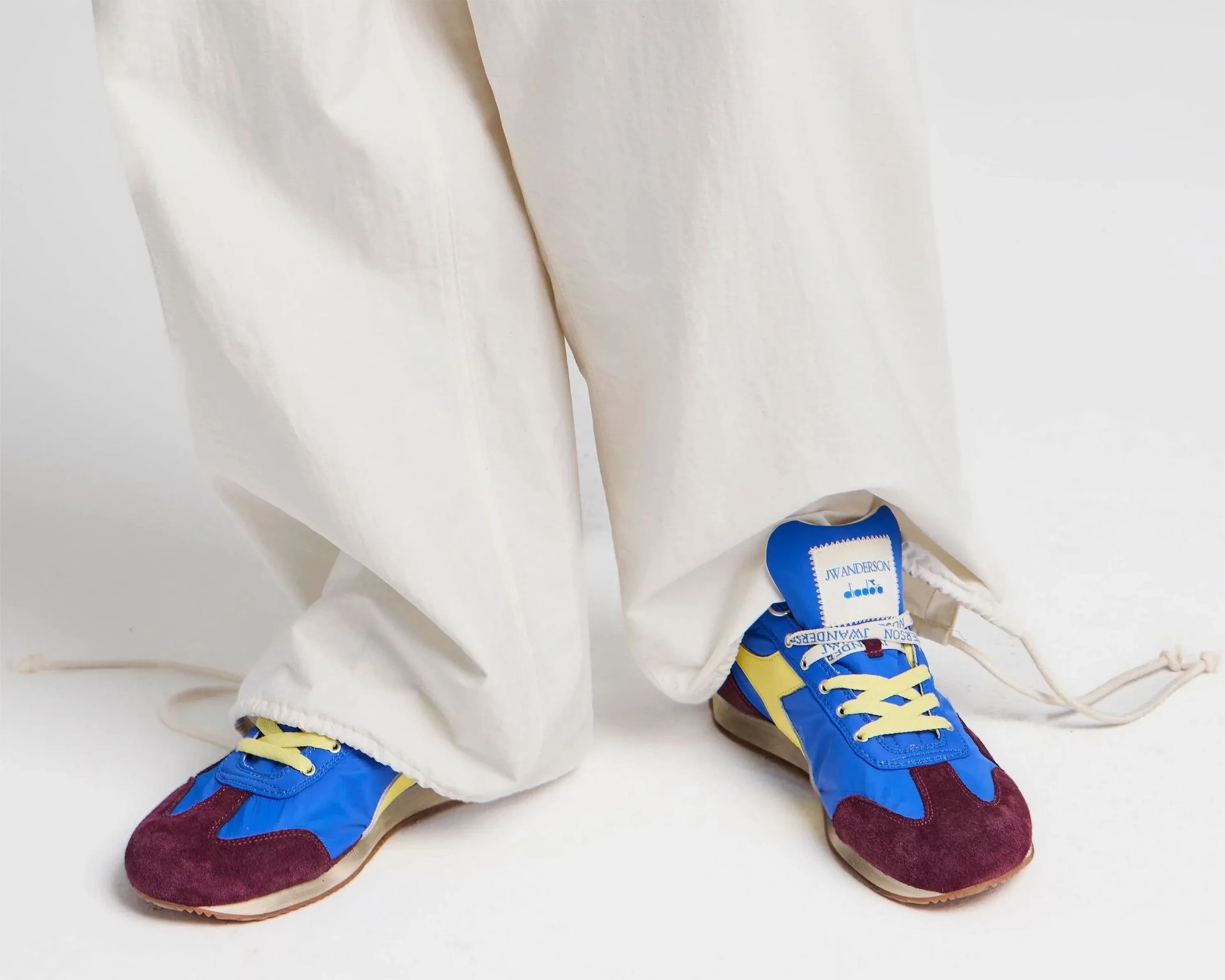Blue, yellow, and burgundy sneakers with yellow laces worn with loose white pants.