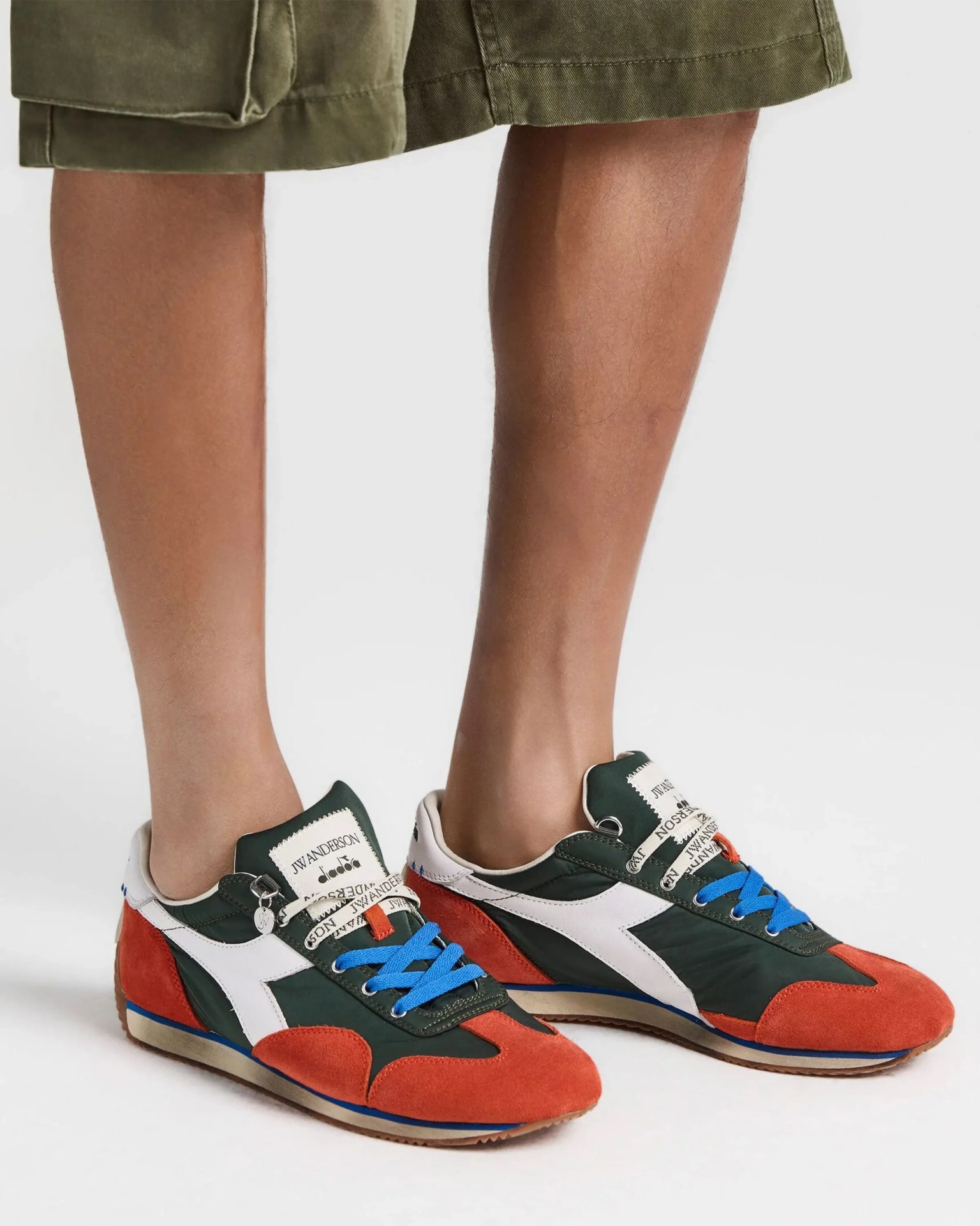 Green, white, and orange sneakers with blue laces worn with olive green shorts.