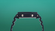Side view of a black digital watch with two silver buttons and a segmented black strap against a green background.