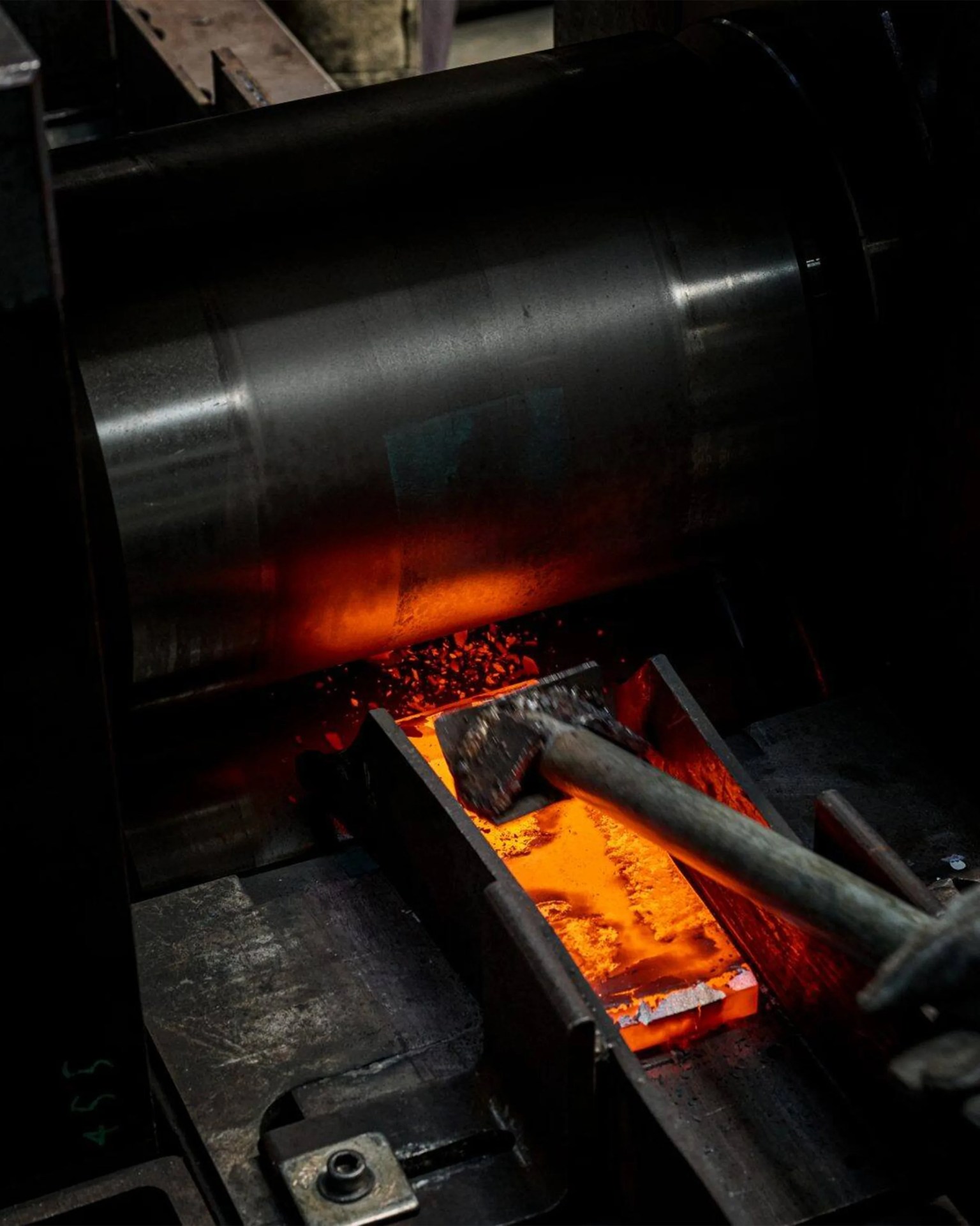 Blacksmith's hammer resting on a glowing orange hot metal piece inside a forge.