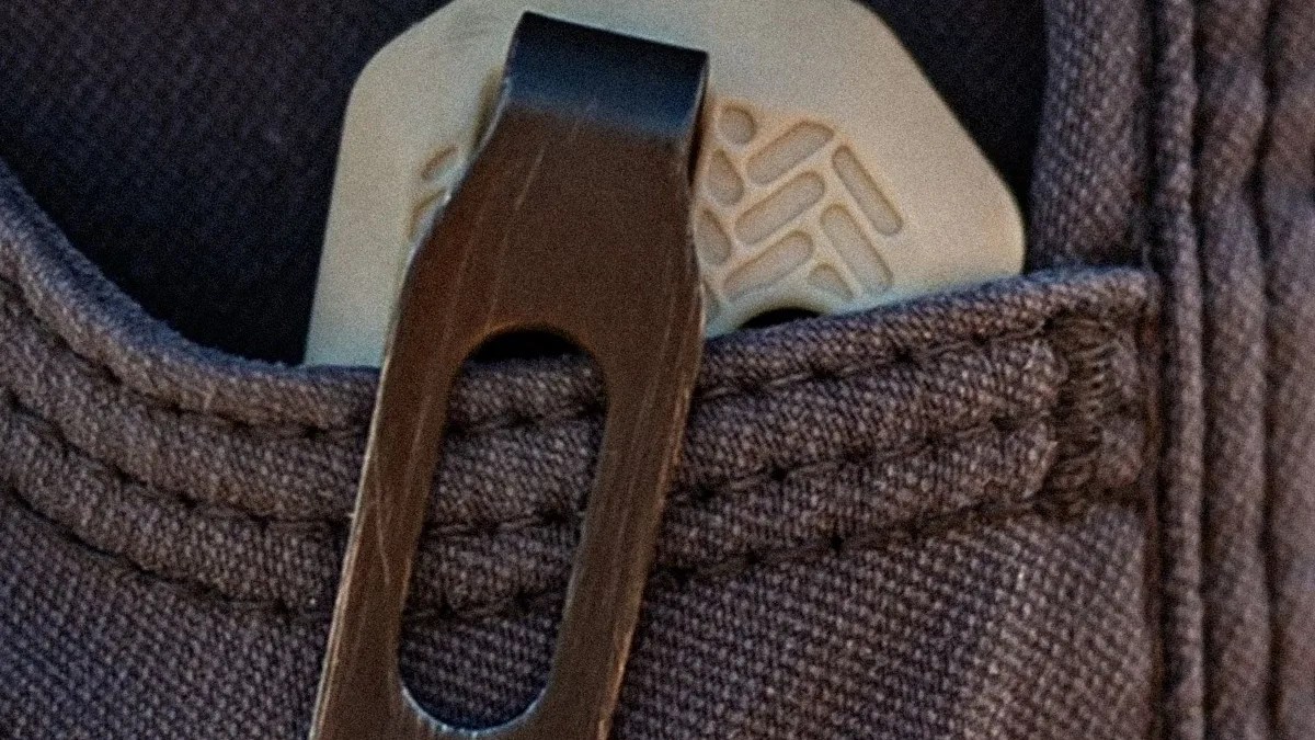 Close-up of a black metal clip attached to a textured dark fabric with a beige object partially visible behind it.