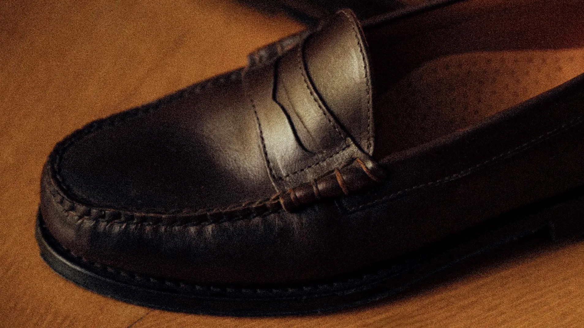 Dark brown leather loafer with visible stitching on a wooden surface.
