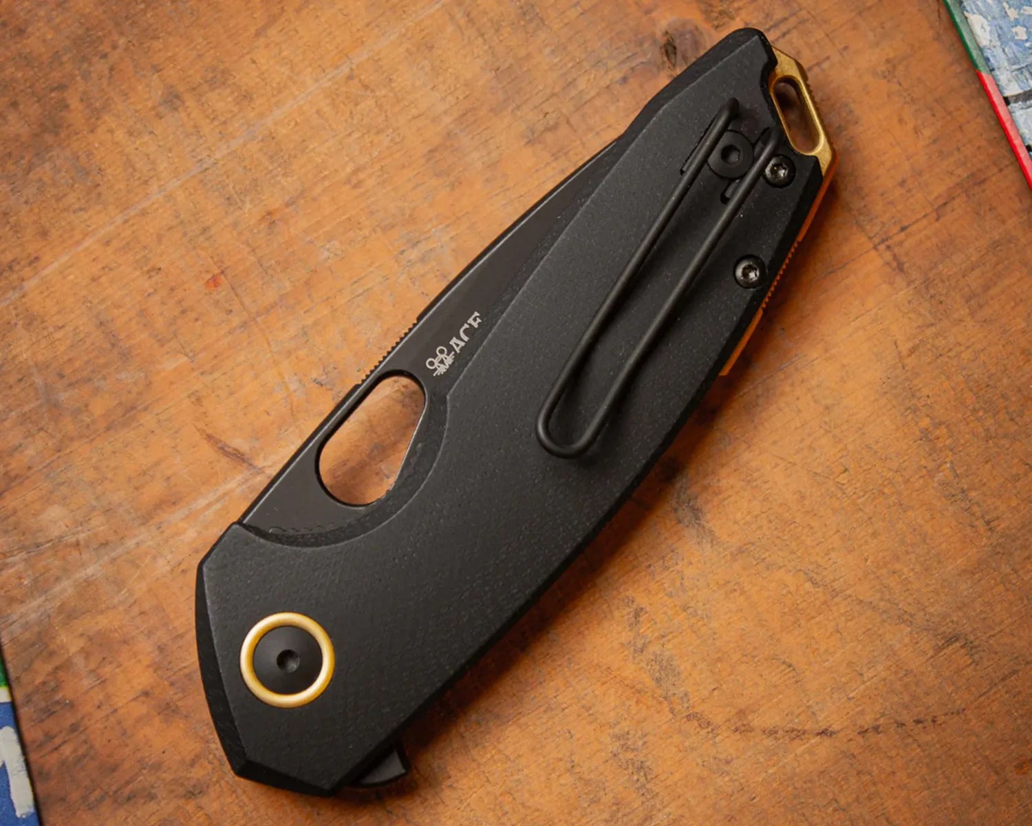 Black folding pocket knife with gold accents and a clip on a wooden surface.