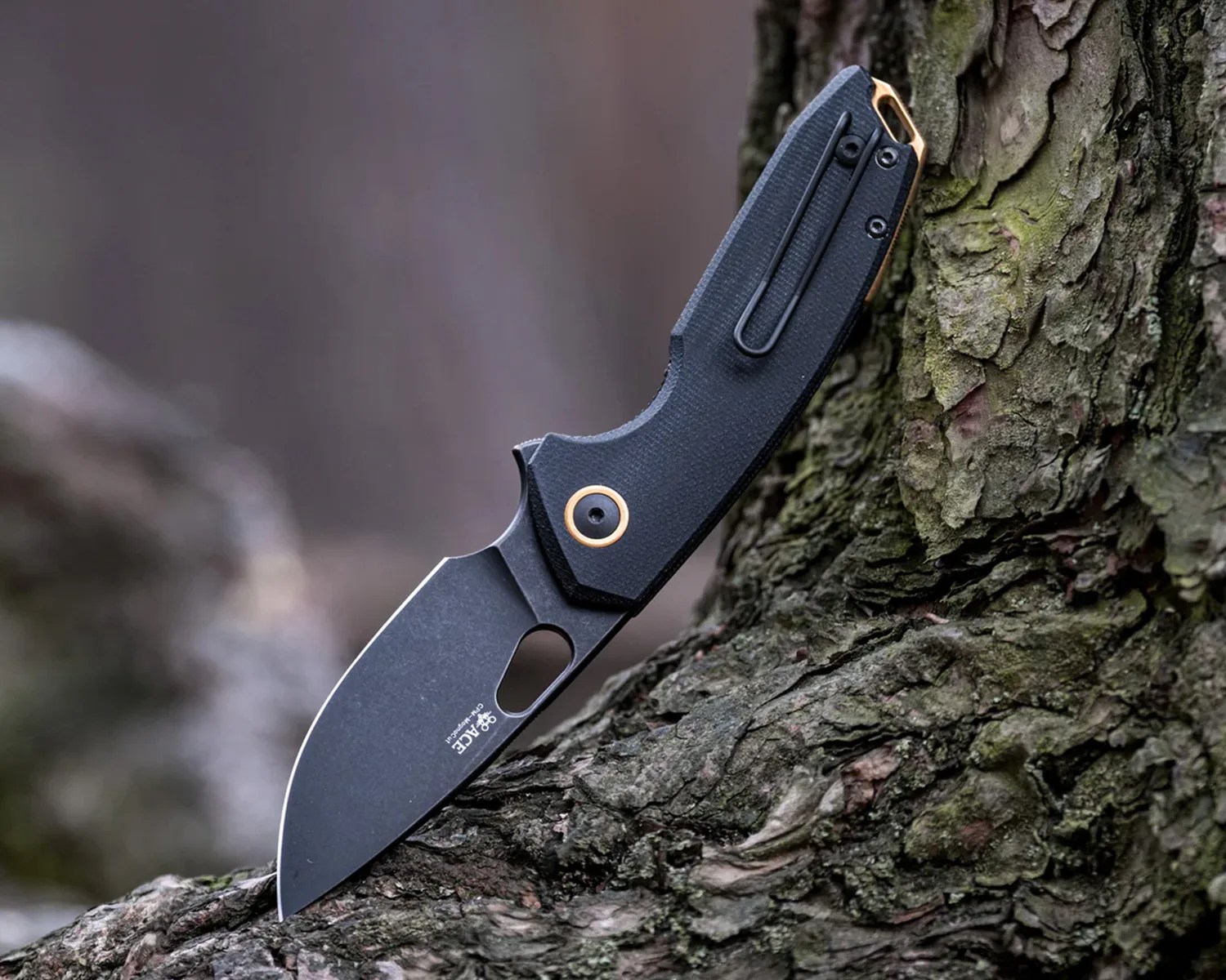 Black folding knife with a textured handle and gold accents stuck in tree bark.