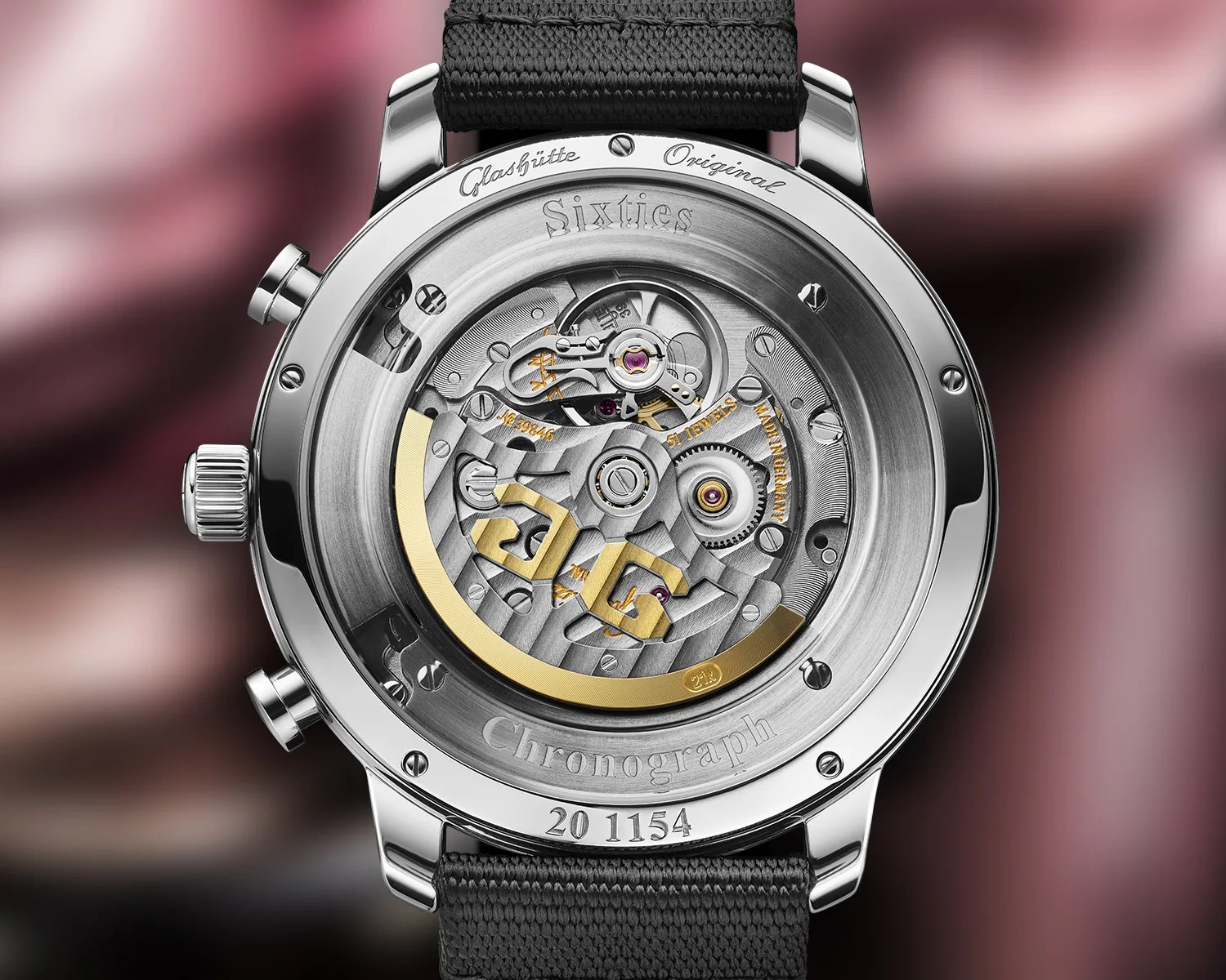 Back of a Glashütte Original Sixties Chronograph watch showing intricate mechanical movement with gold accents and black fabric strap.