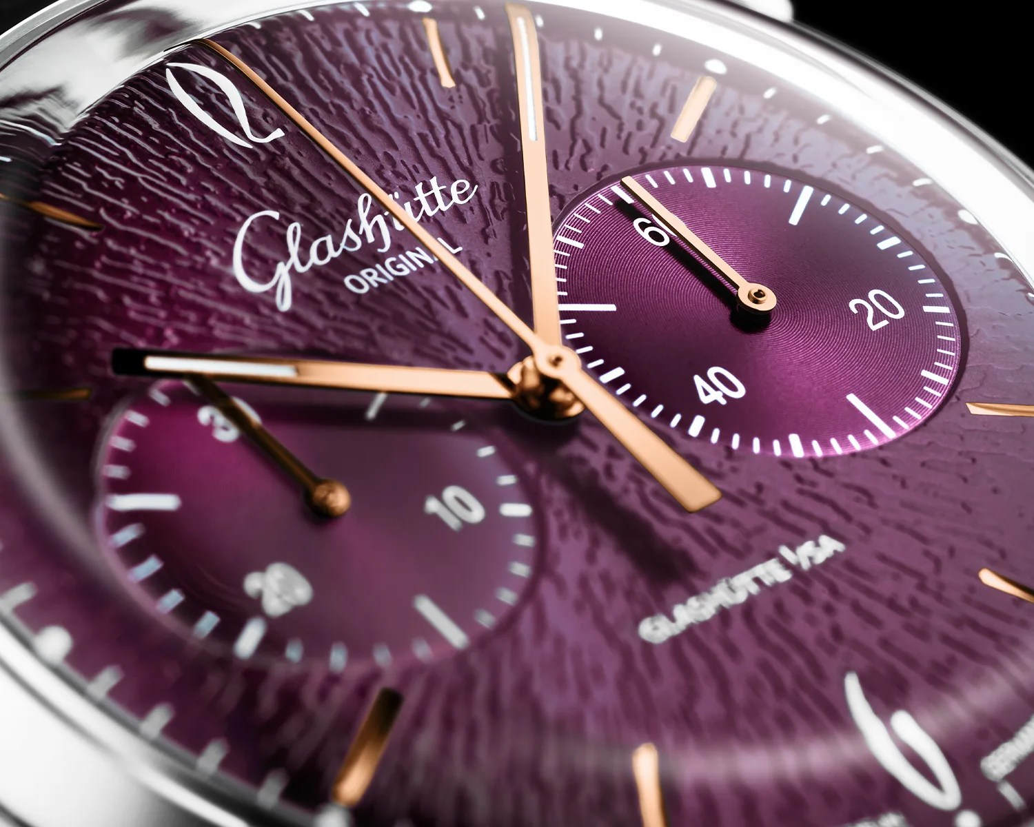 Close-up of a purple textured Glashütte Original watch dial with gold hands and two subdials.