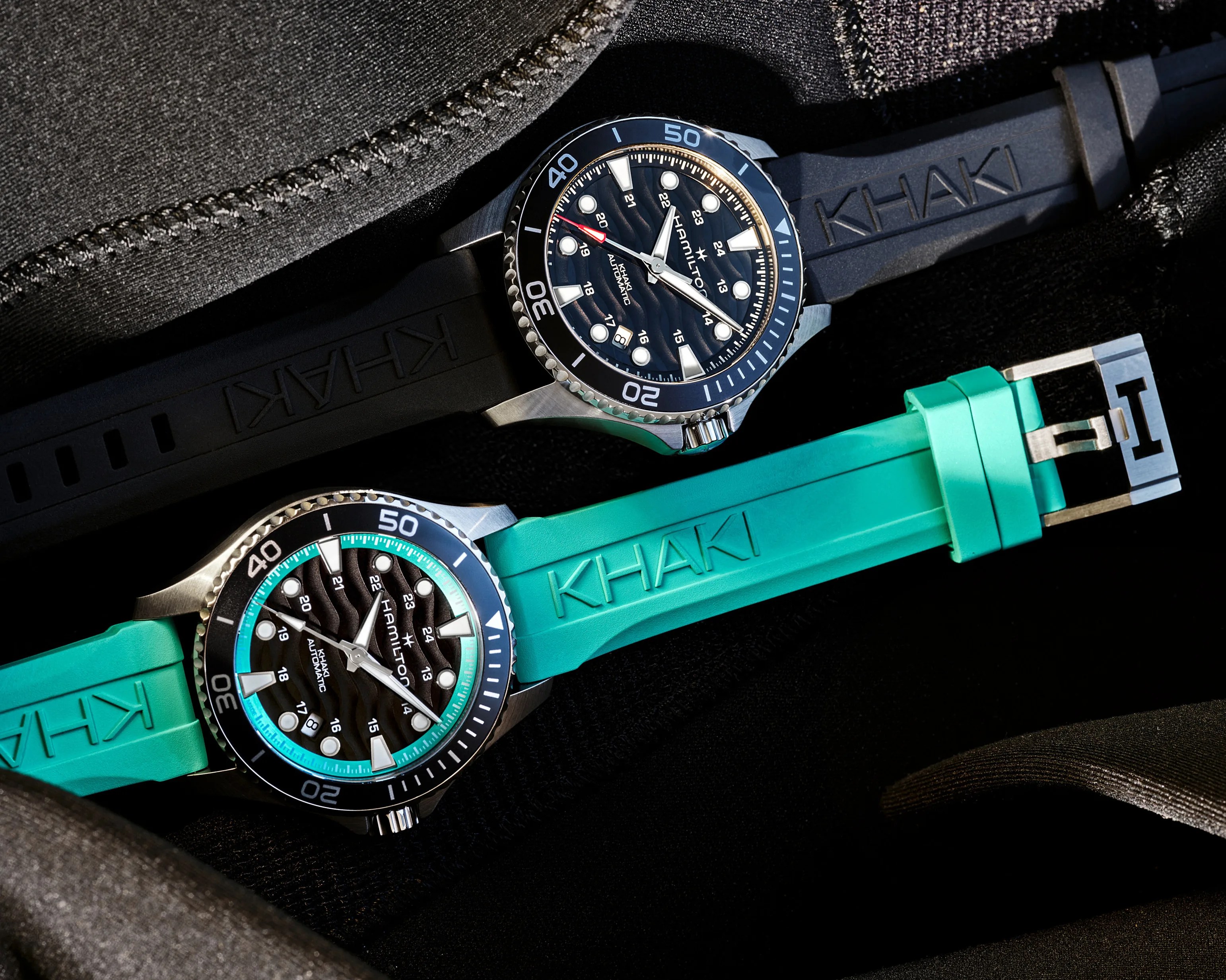 Two Hamilton Khaki automatic watches with black dials and wave patterns, one with a black strap and one with a turquoise strap.