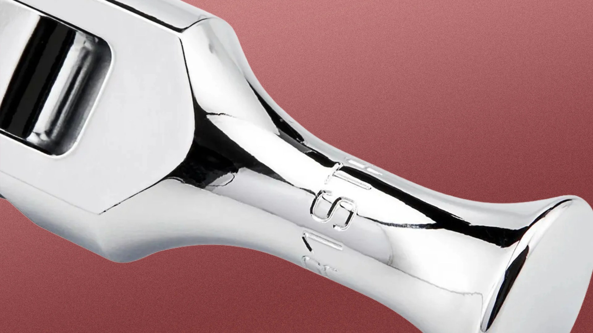 Close-up of a shiny chrome wrench head on a textured reddish-brown background.