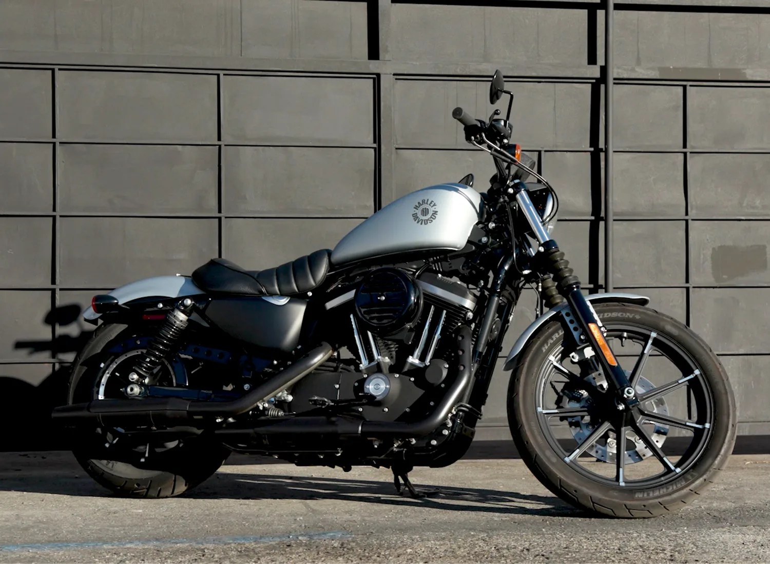 Silver and black Harley-Davidson motorcycle parked on concrete in front of a gray paneled wall.