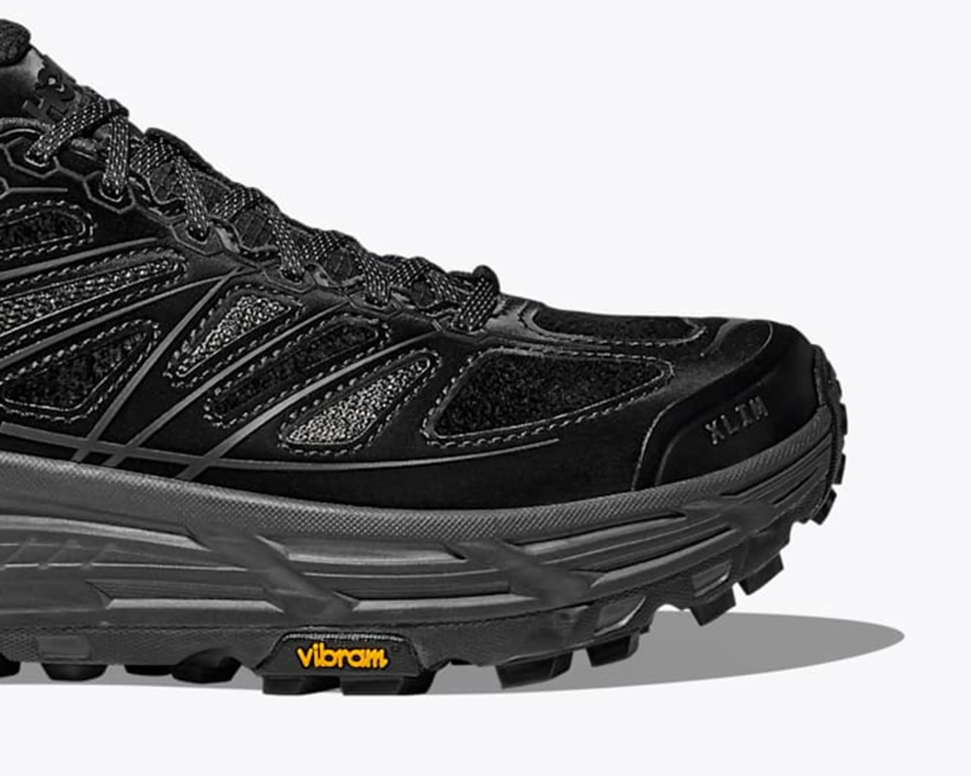 Black athletic shoe with mesh and synthetic overlays, gray midsole, and Vibram outsole.