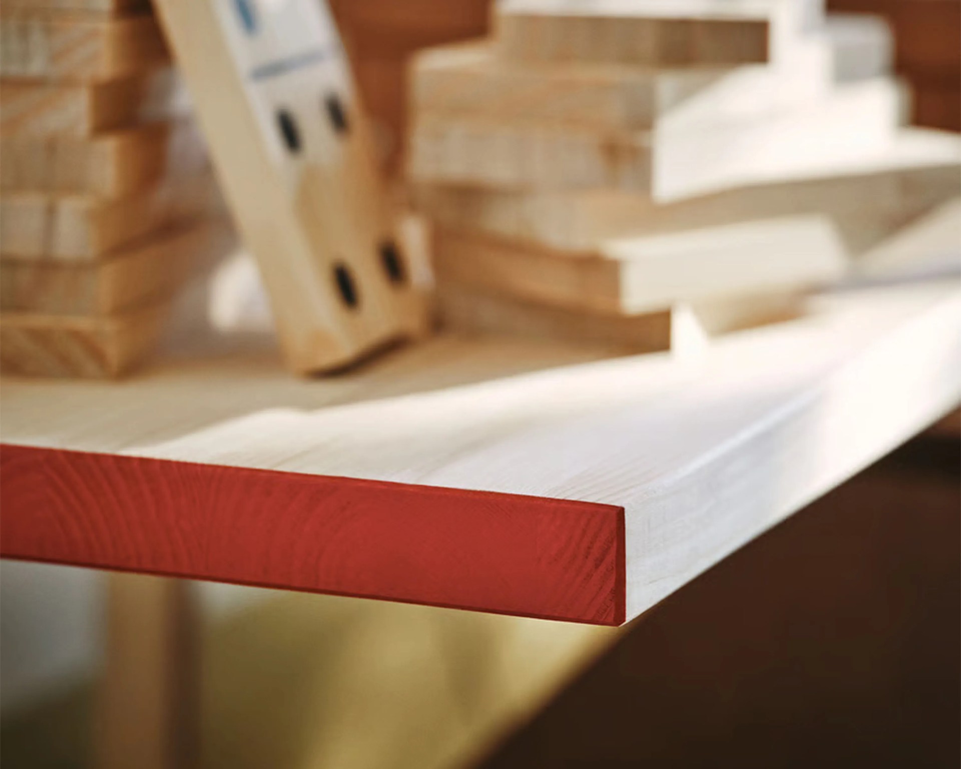 Close-up of a wooden board with a red-painted end and blurred wooden blocks in the background.