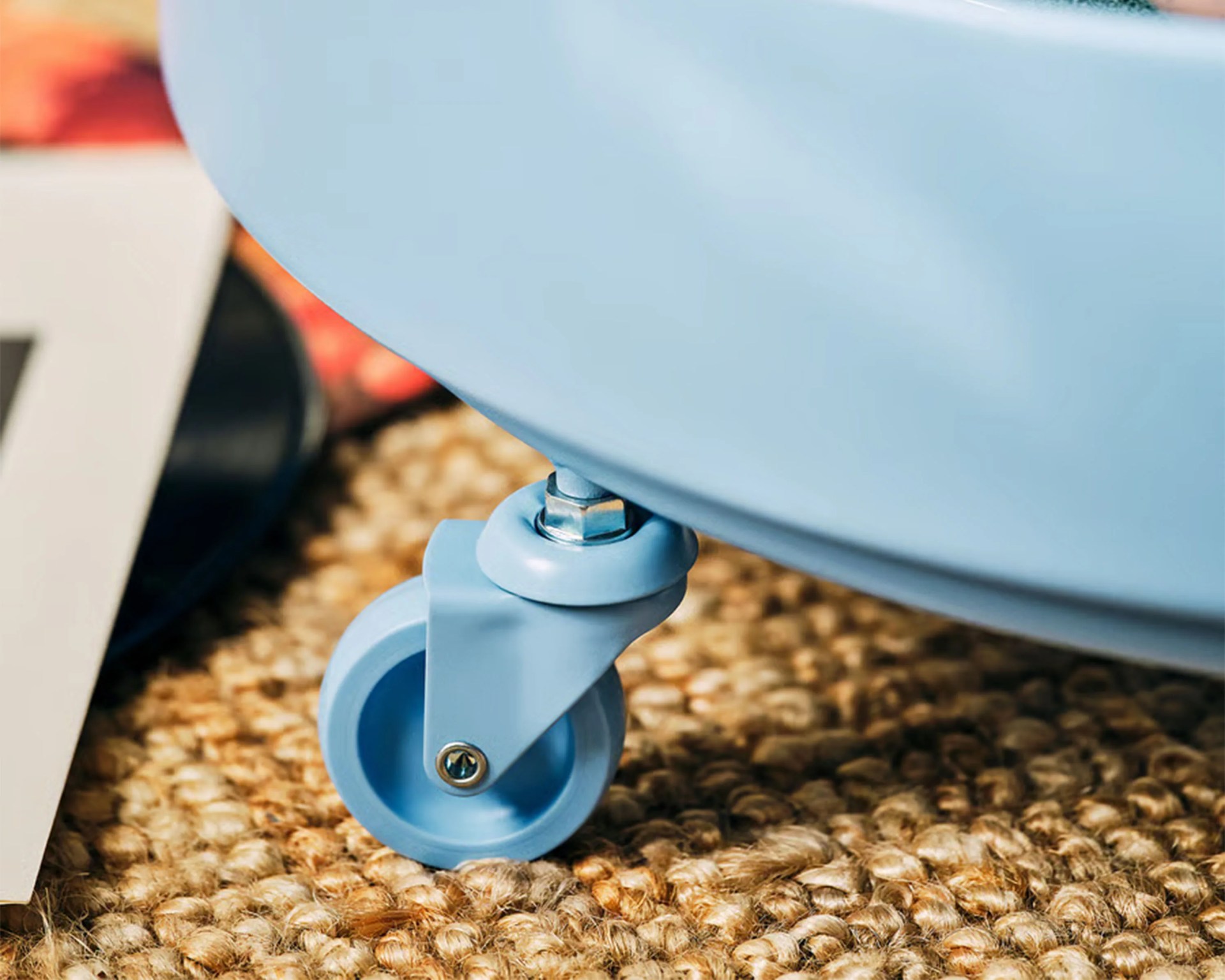 Close-up of a light blue caster wheel attached to a piece of furniture on a woven natural fiber rug.