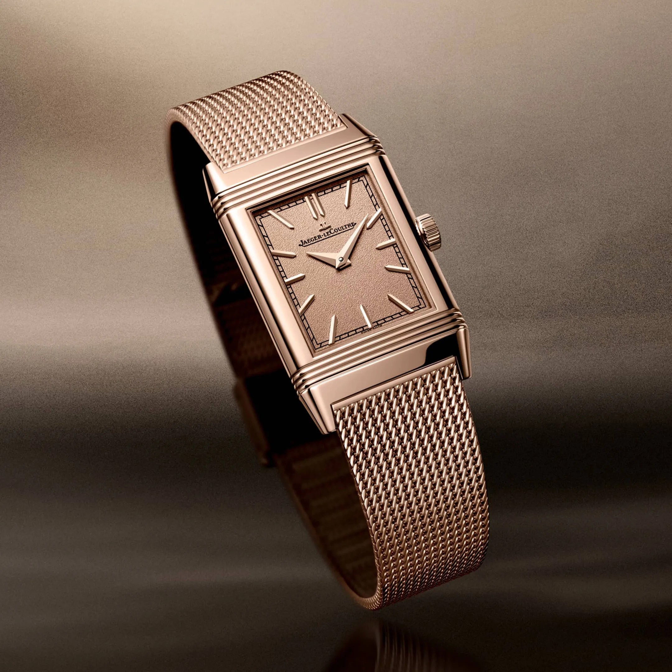 Rectangular rose gold Jaeger-LeCoultre watch with textured dial and mesh bracelet on a gradient brown background.