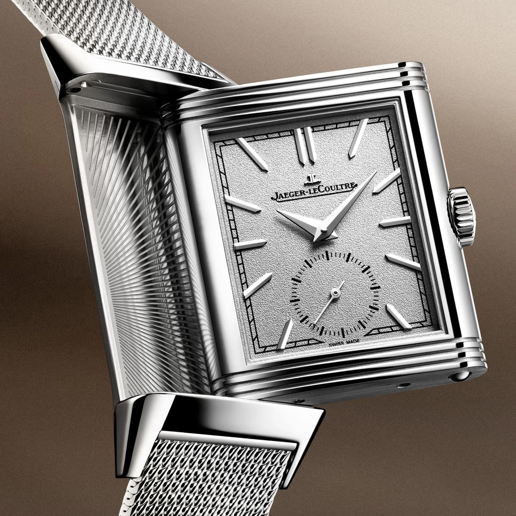Close-up of a silver Jaeger-LeCoultre rectangular watch with a textured dial and mesh metal strap.