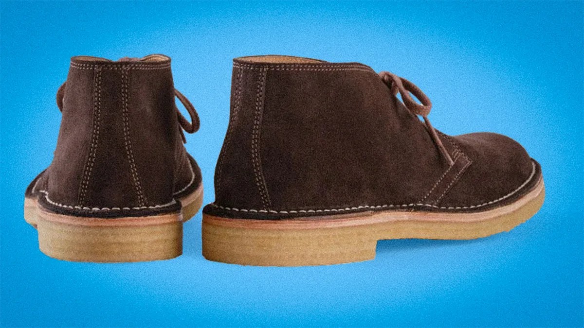 Pair of brown suede desert boots with beige crepe soles on a blue background.