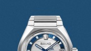 Silver Seiko wristwatch with blue and white dial and metal link bracelet on a blue background.