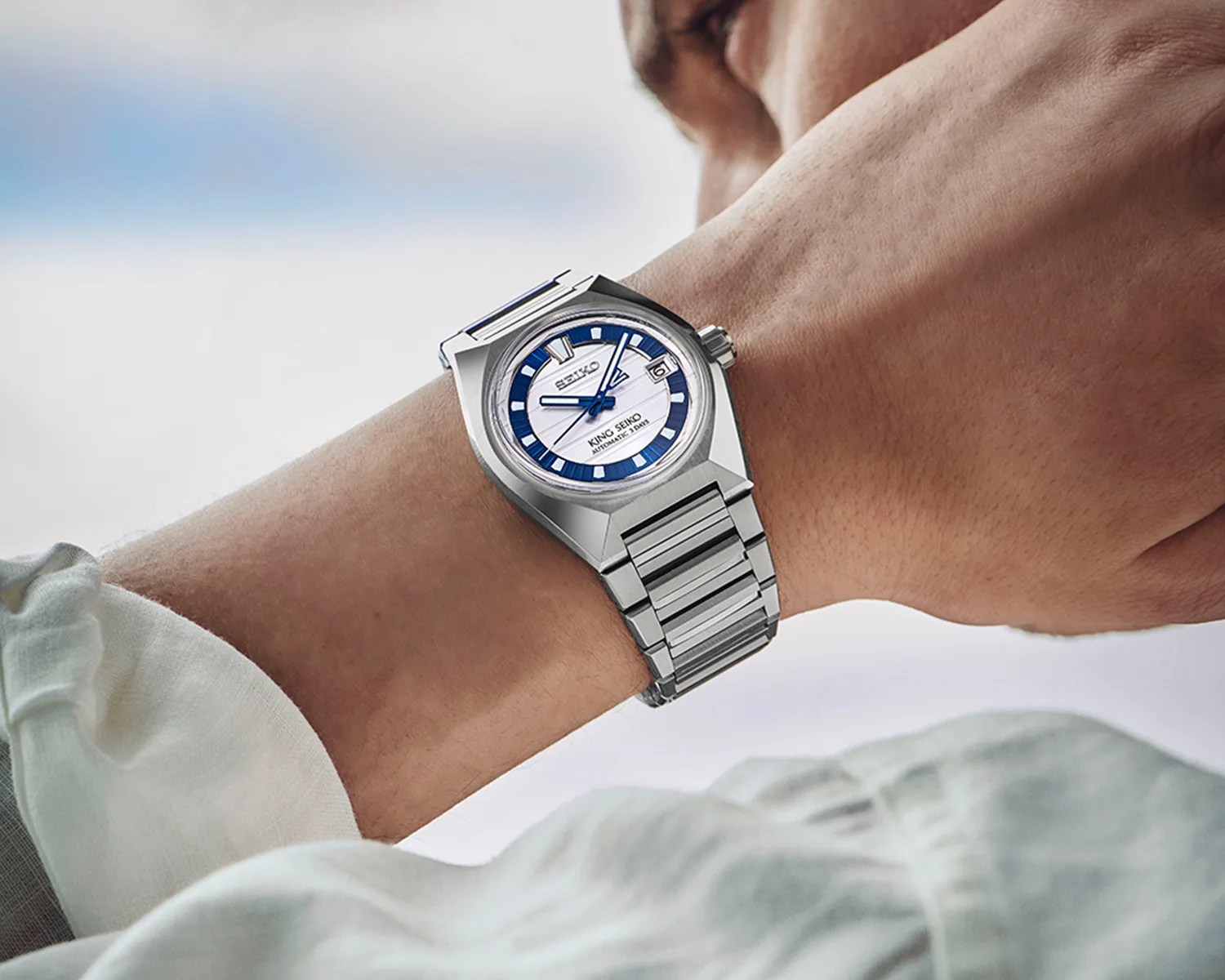 Silver stainless steel wristwatch with a white and blue dial worn on a wrist.